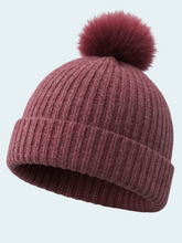 Burgundy knit beanie with a pom-pom on a light gray background