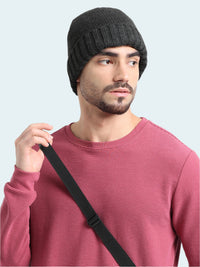 Man wearing a black knit beanie and pink sweater with a black strap over his shoulder on a white background