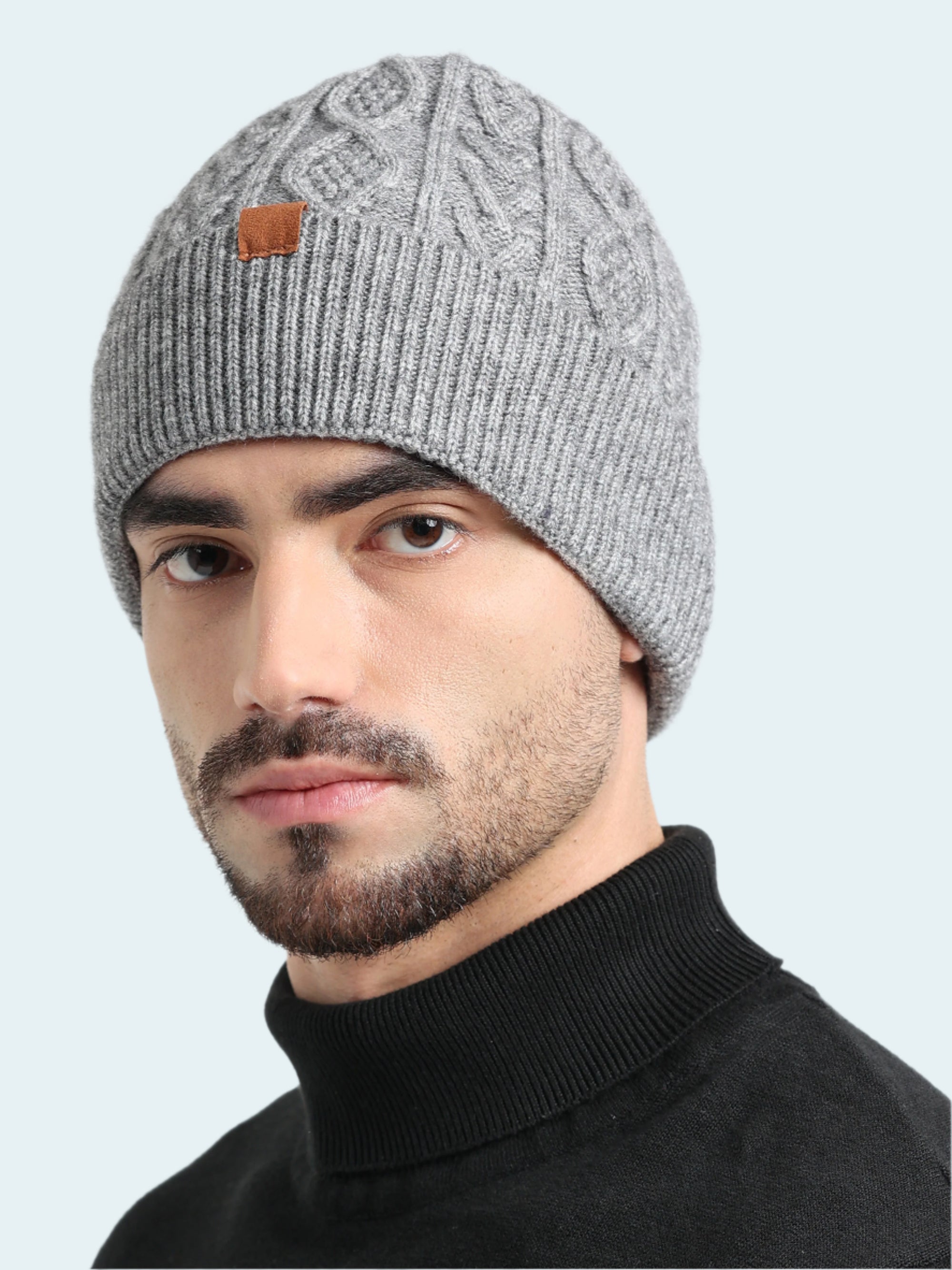 Man wearing a gray knit beanie with a brand logo on a white background
