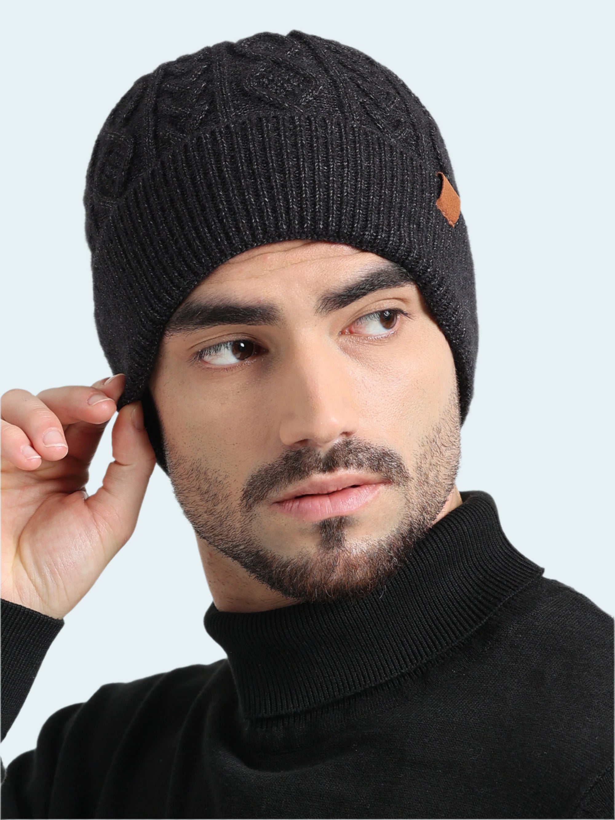 Man wearing a black knit beanie with a brand logo on a light gray background