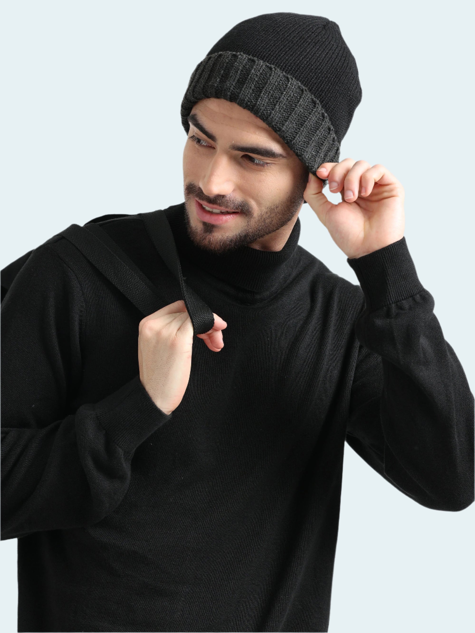 Man wearing a black knit beanie and black hoodie against a light gray background