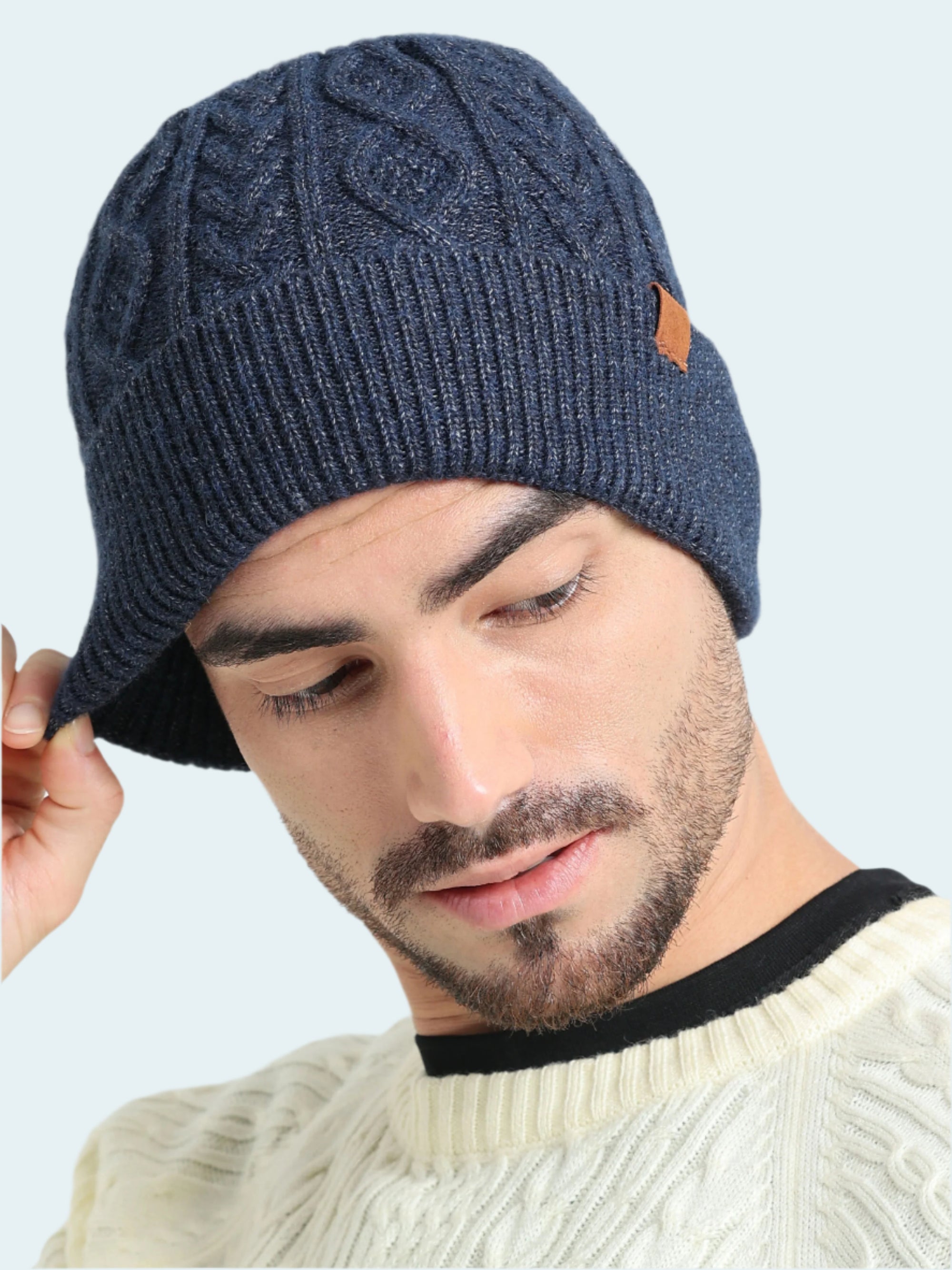 Man wearing a blue knitted beanie with a brand logo on a light gray background