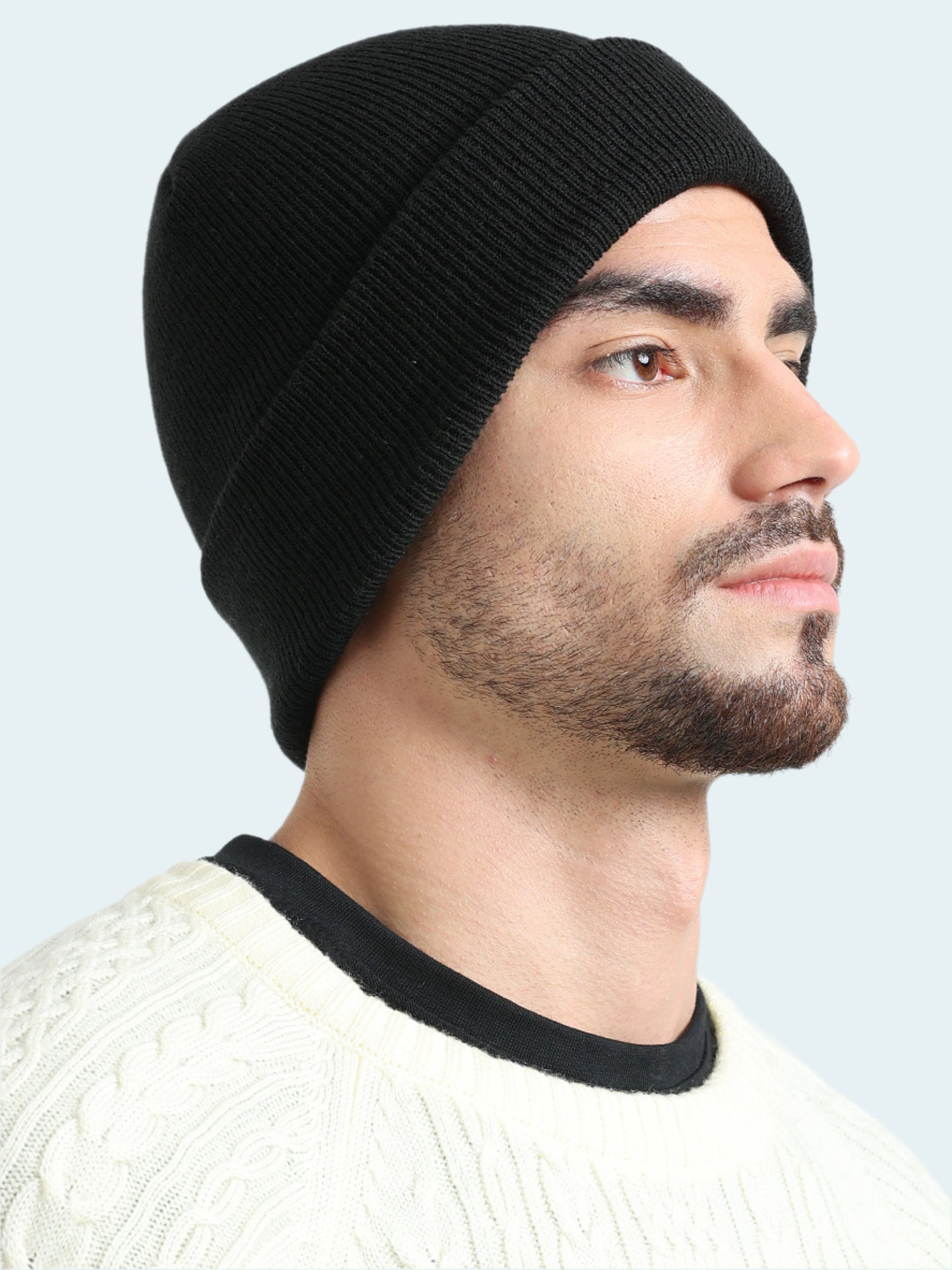 Man wearing a black knit beanie and white sweater on a light gray background