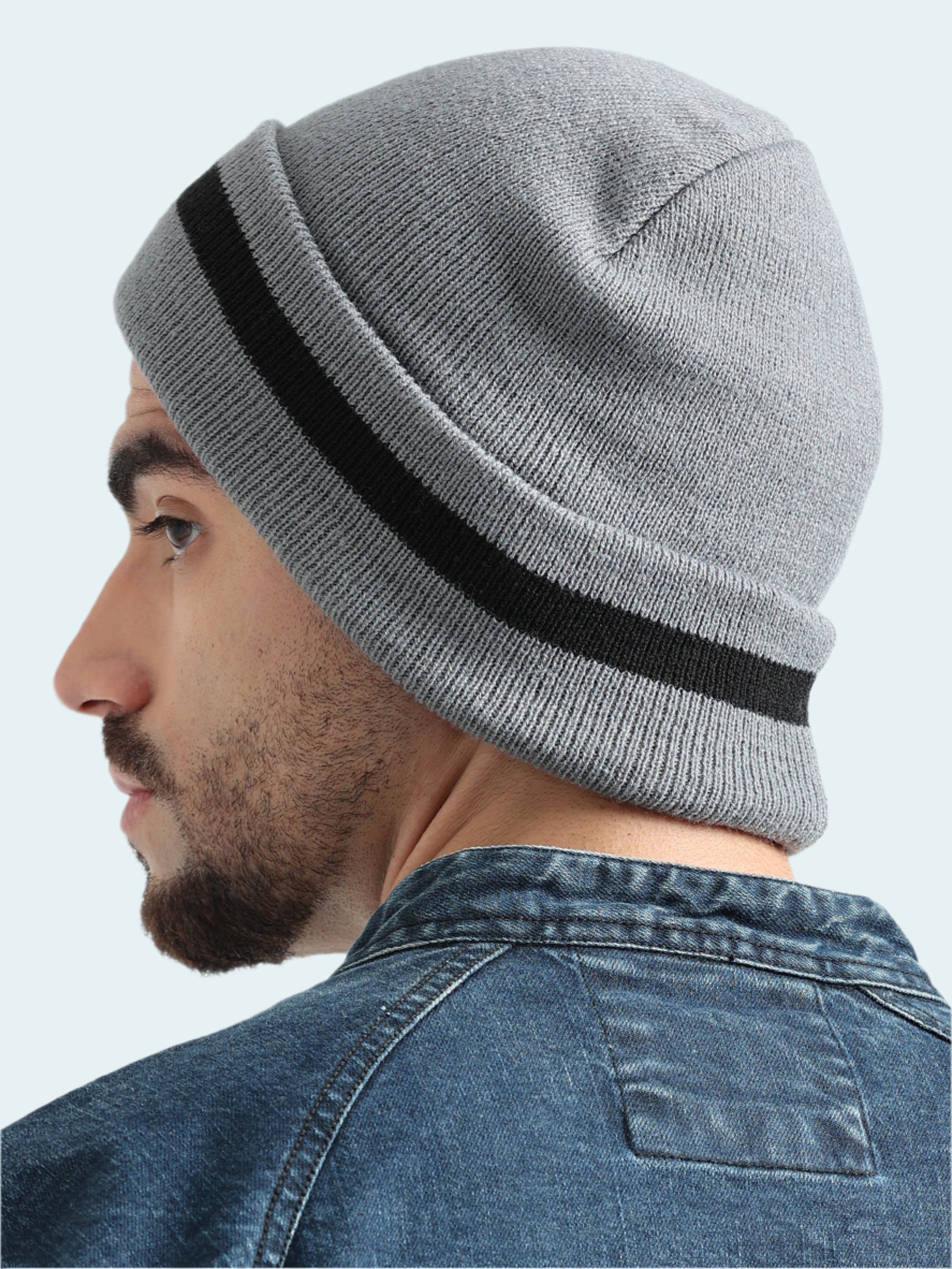 Person wearing a gray knit beanie with a black stripe on a white background