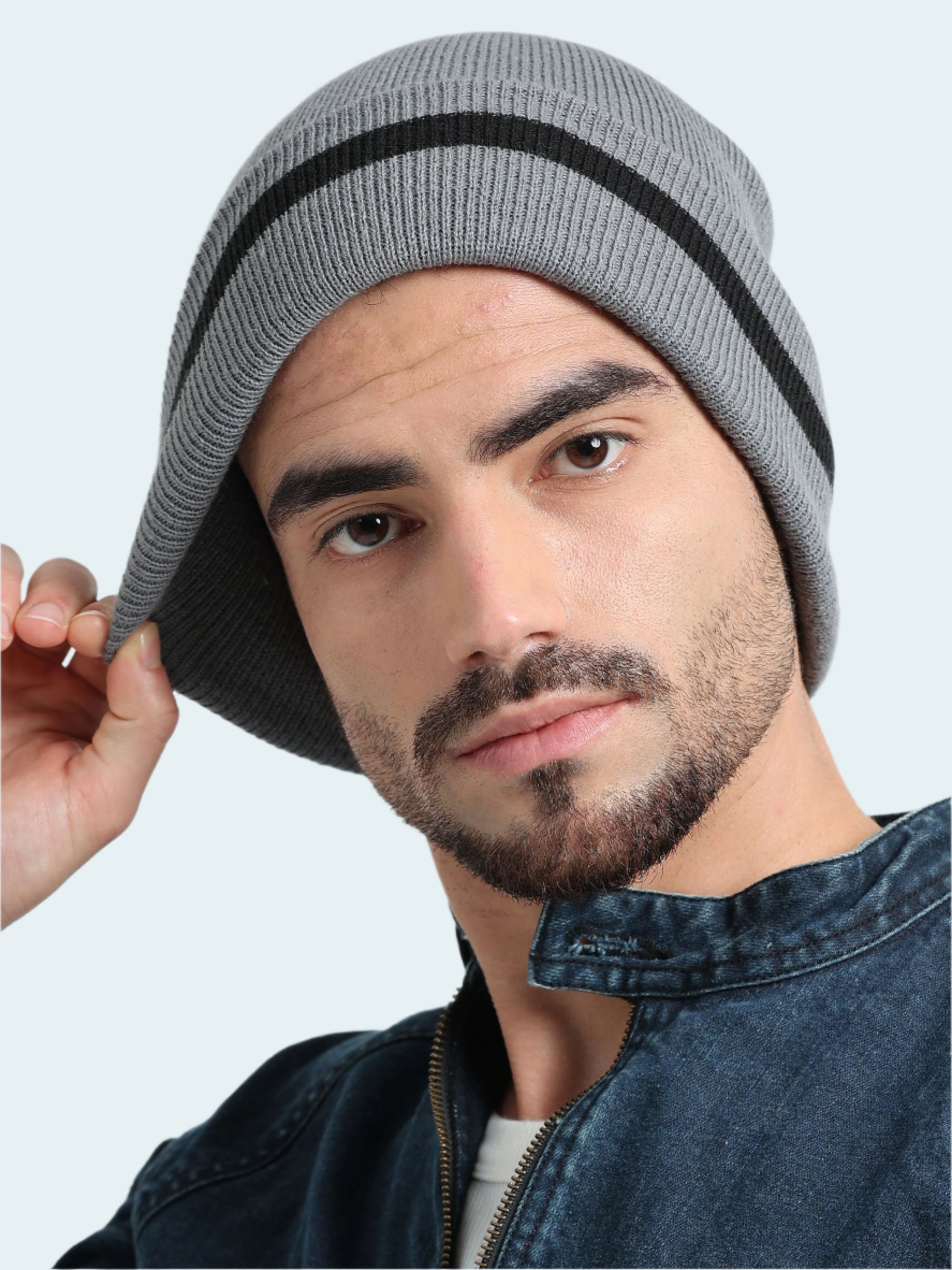 Man wearing a gray knit beanie with a black stripe on a light gray background