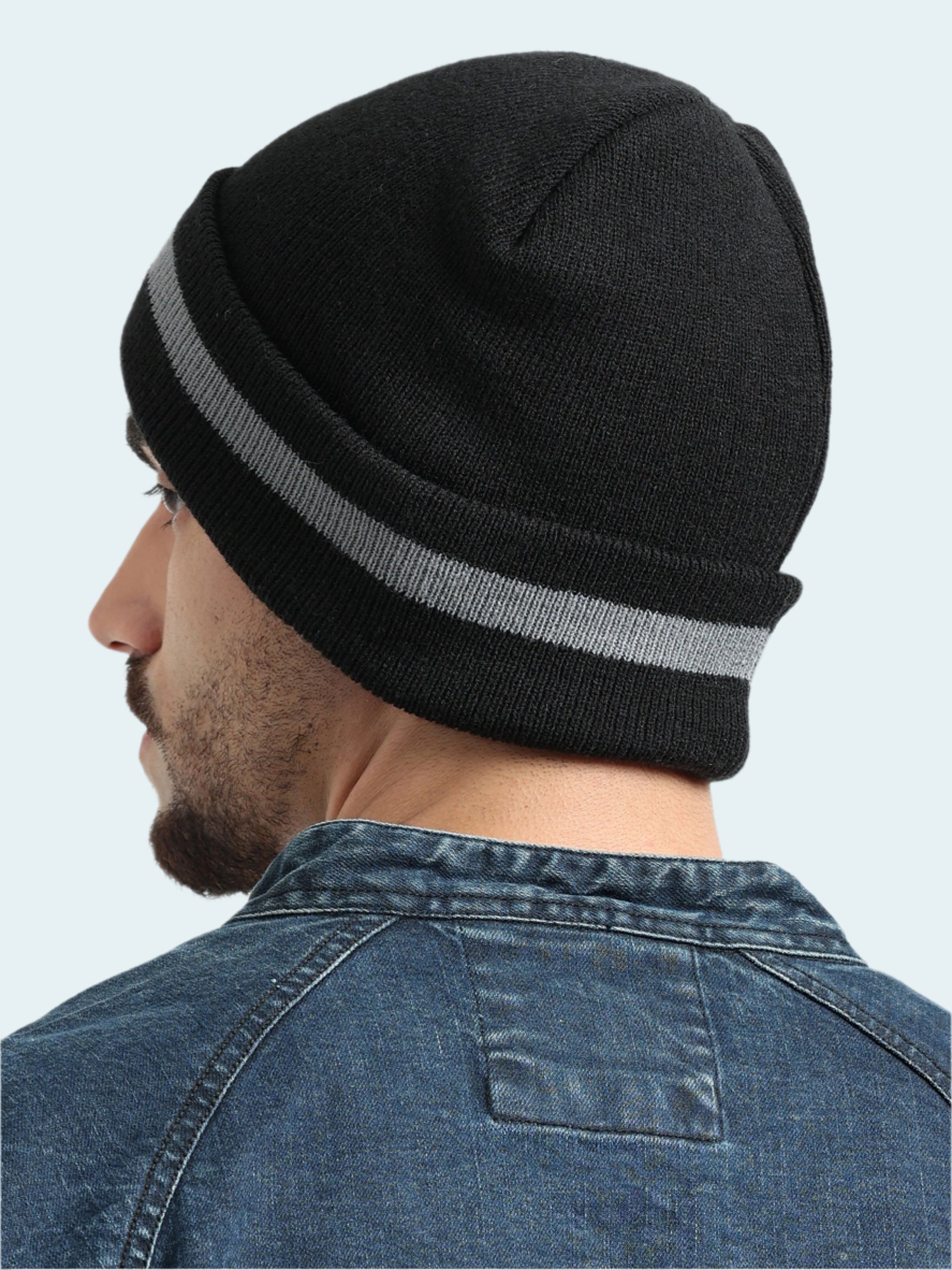Person wearing a black beanie with a gray stripe on a light gray background