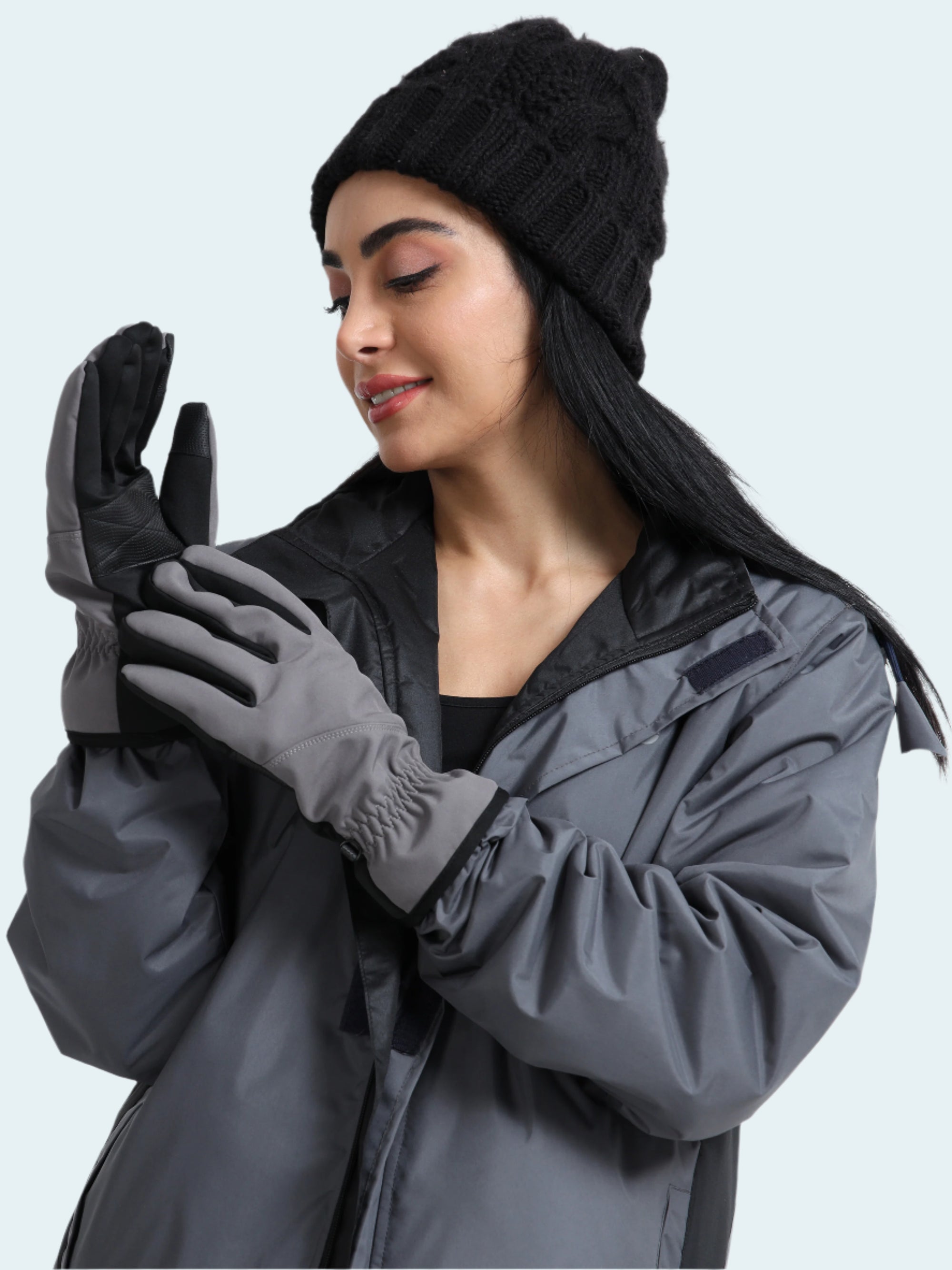 Woman wearing a gray coat, black beanie, and gloves on a white background