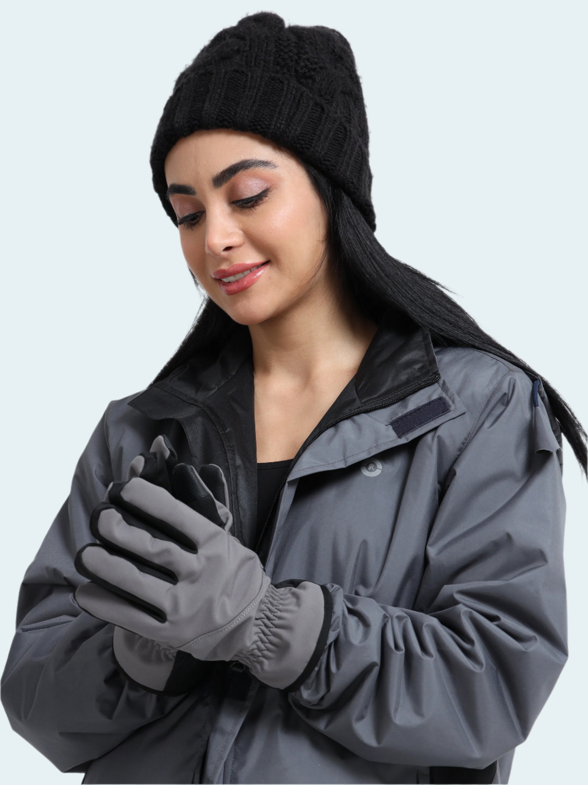 Woman wearing a gray jacket, black beanie, and gloves on a light gray background