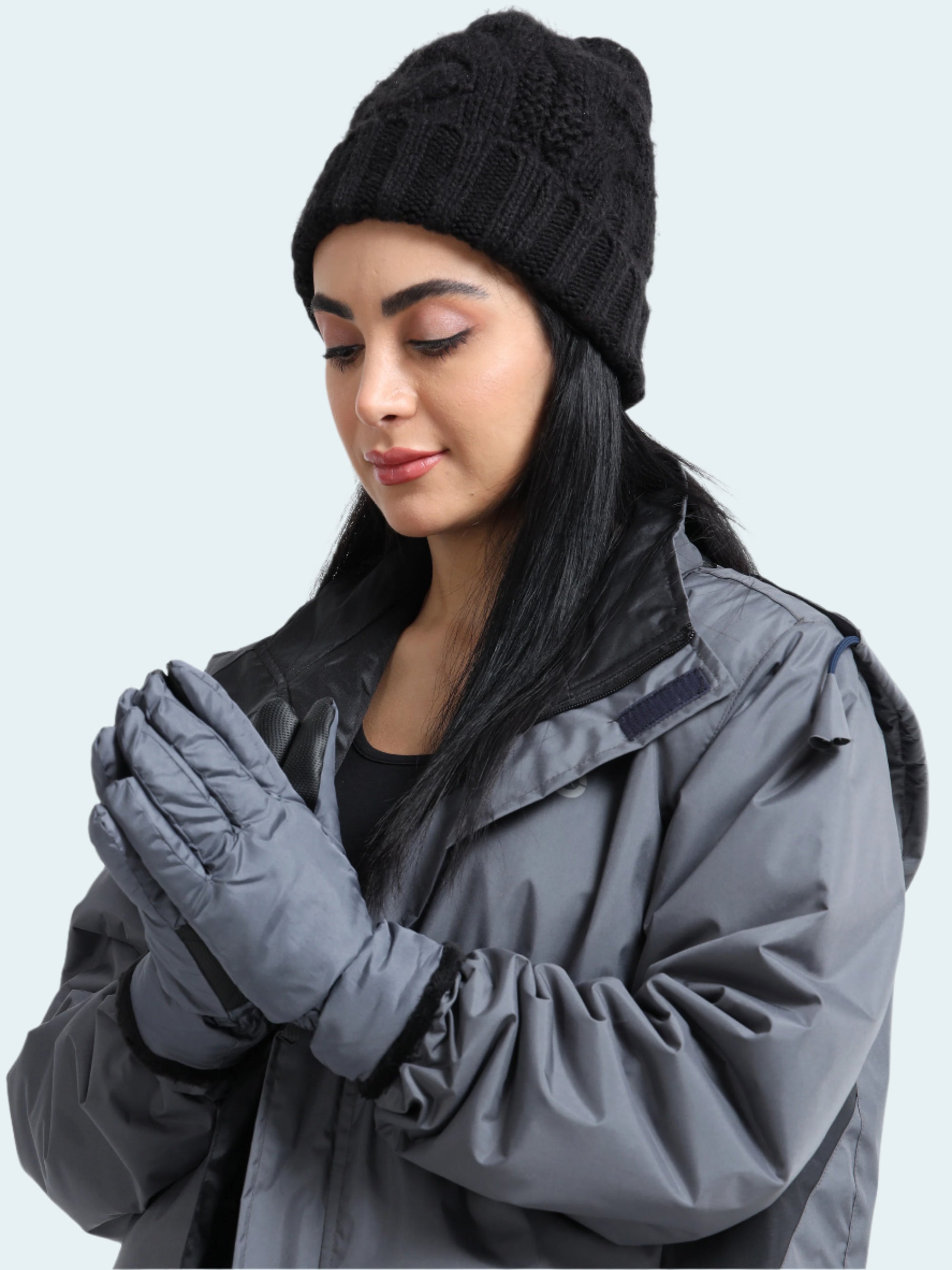 Woman wearing a black knit beanie, gray jacket, and gloves on a white background