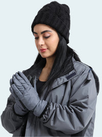Woman wearing a black knit beanie, gray jacket, and gloves on a white background