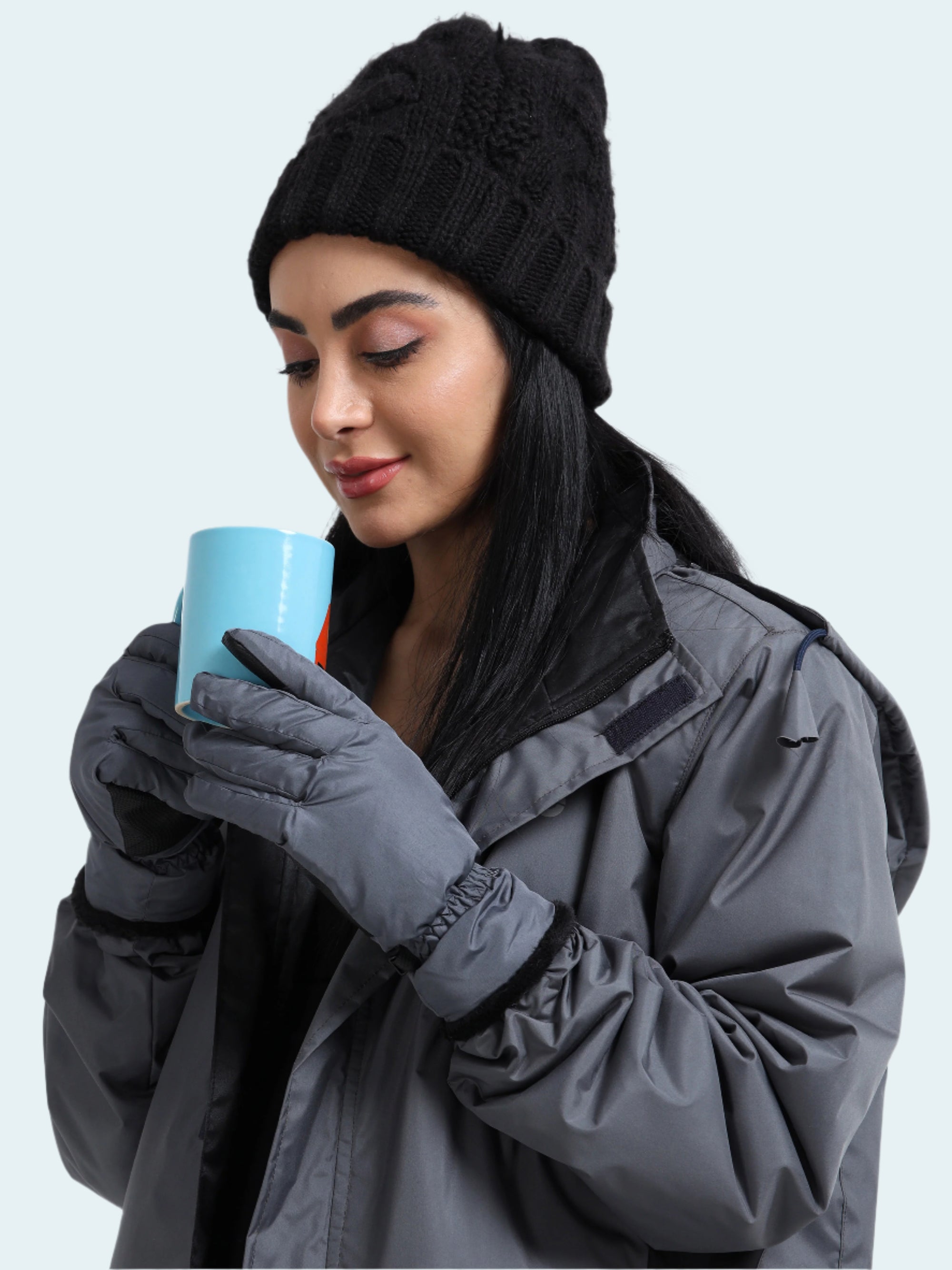Woman in winter clothing holding a blue mug against a white background