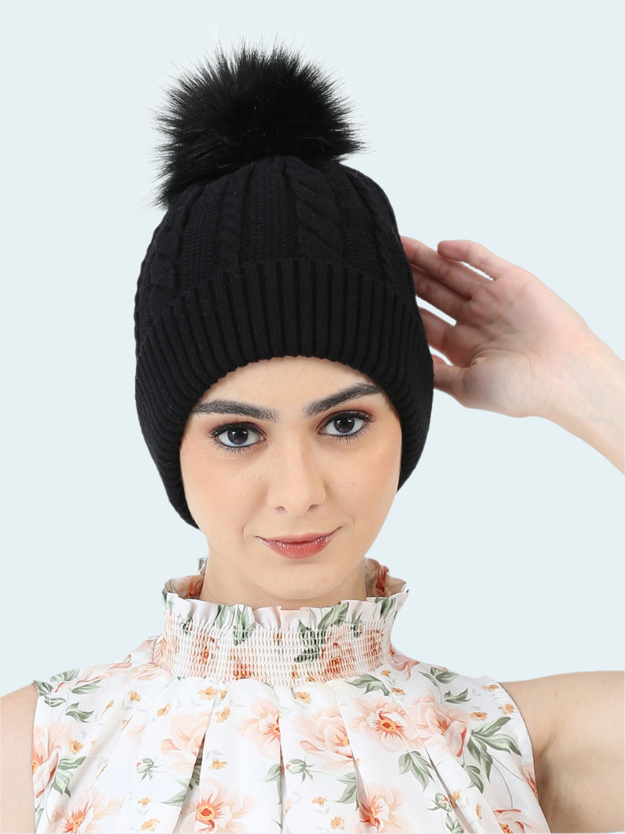 Black knit beanie with a pom-pom worn by a person on a white background