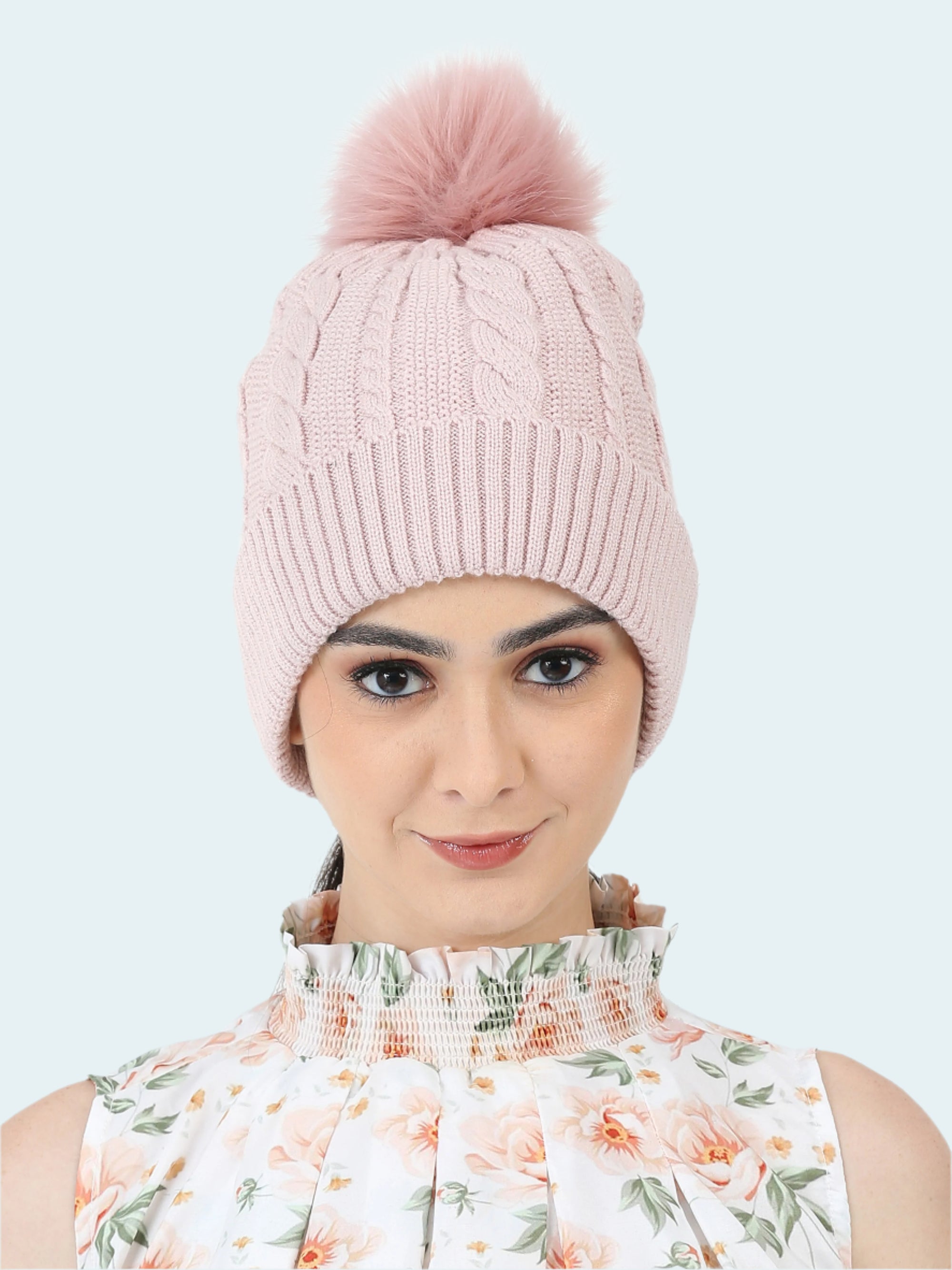Pink knitted beanie with a pom-pom worn by a person on a white background