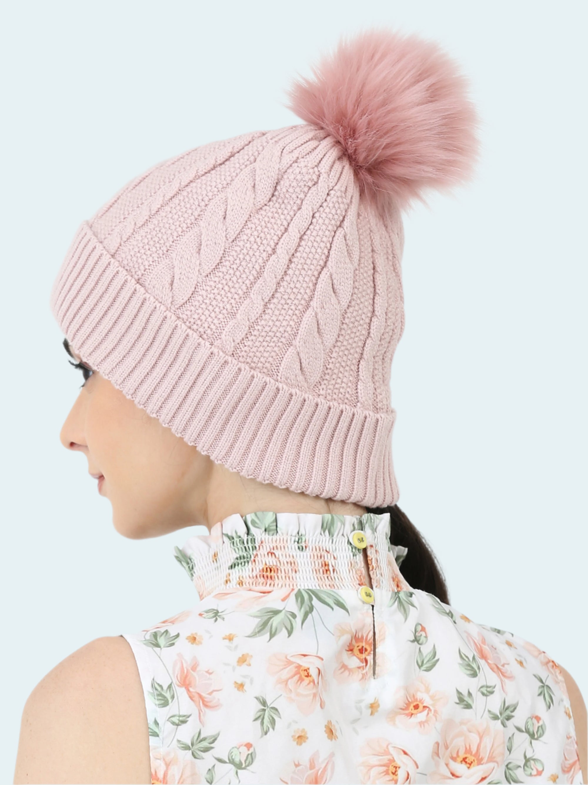 Pink knitted beanie with a fluffy pom-pom worn by a person against a white background