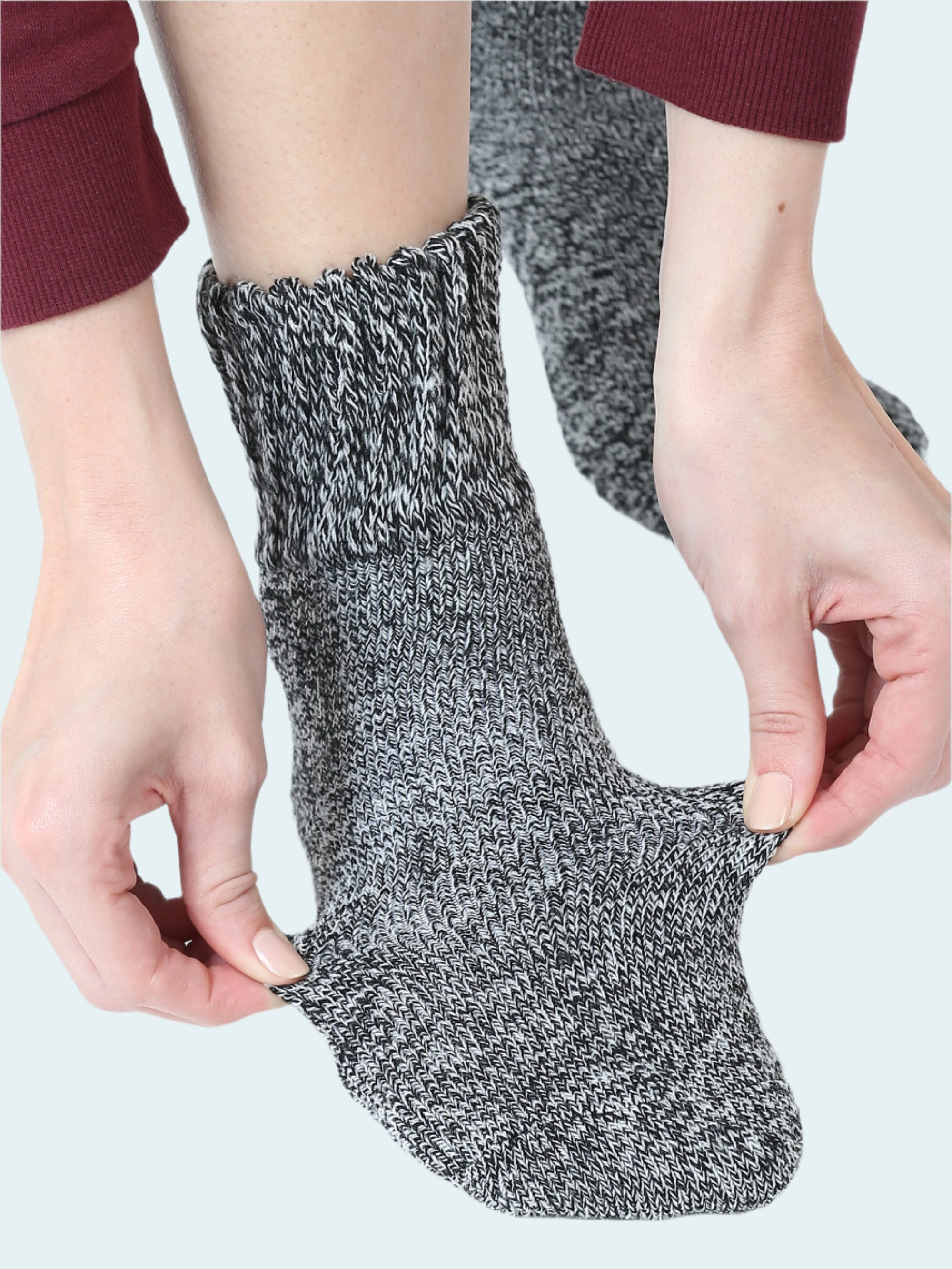 Person wearing a gray and black textured sock with hands adjusting it on a white background