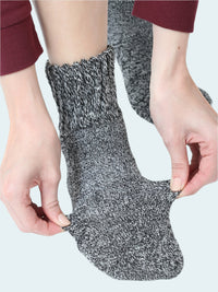 Person wearing a gray and black textured sock with hands adjusting it on a white background