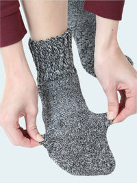 Person wearing a gray and black textured sock with hands adjusting it on a white background
