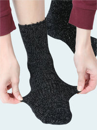 Person wearing black chenille socks with a textured pattern on a white background