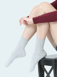 Person wearing gray socks sitting on a stool with a white background