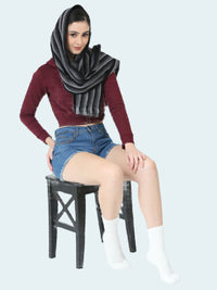 Woman wearing a dark gray scarf, maroon sweater, denim shorts, and white socks sitting on a black stool against a white background.