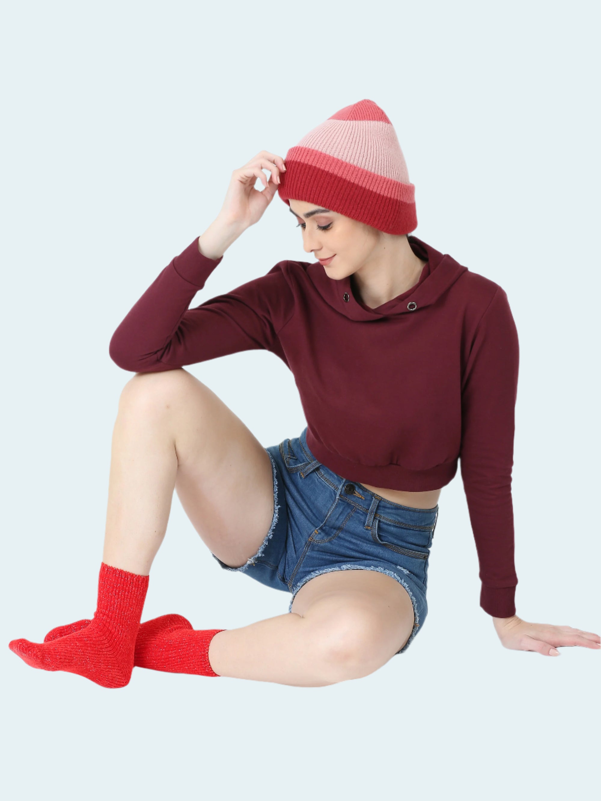 Woman wearing a burgundy hoodie, denim shorts, and red socks with a white background
