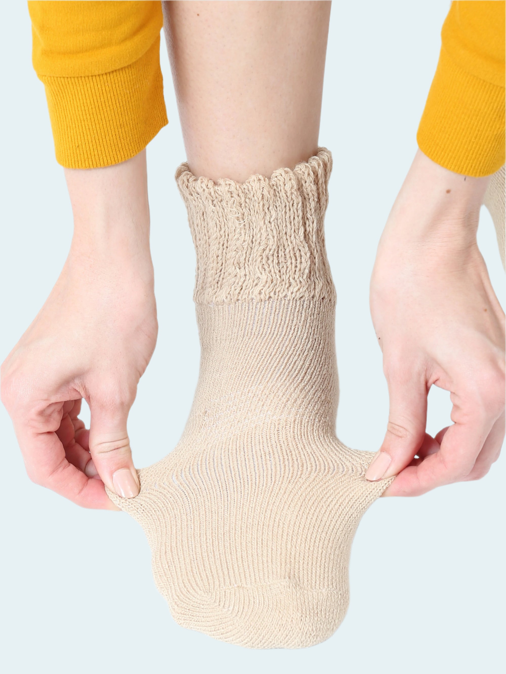 Person wearing a beige sock with hands adjusting it on a white background