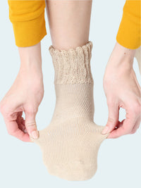 Person wearing a beige sock with hands adjusting it on a white background