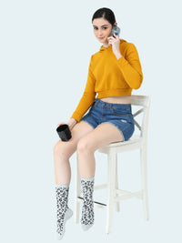 This image features a stylish young woman seated on a chair, She is wearing a vibrant mustard-colored crop top and denim shorts, adding a casual yet trendy touch to the scene.