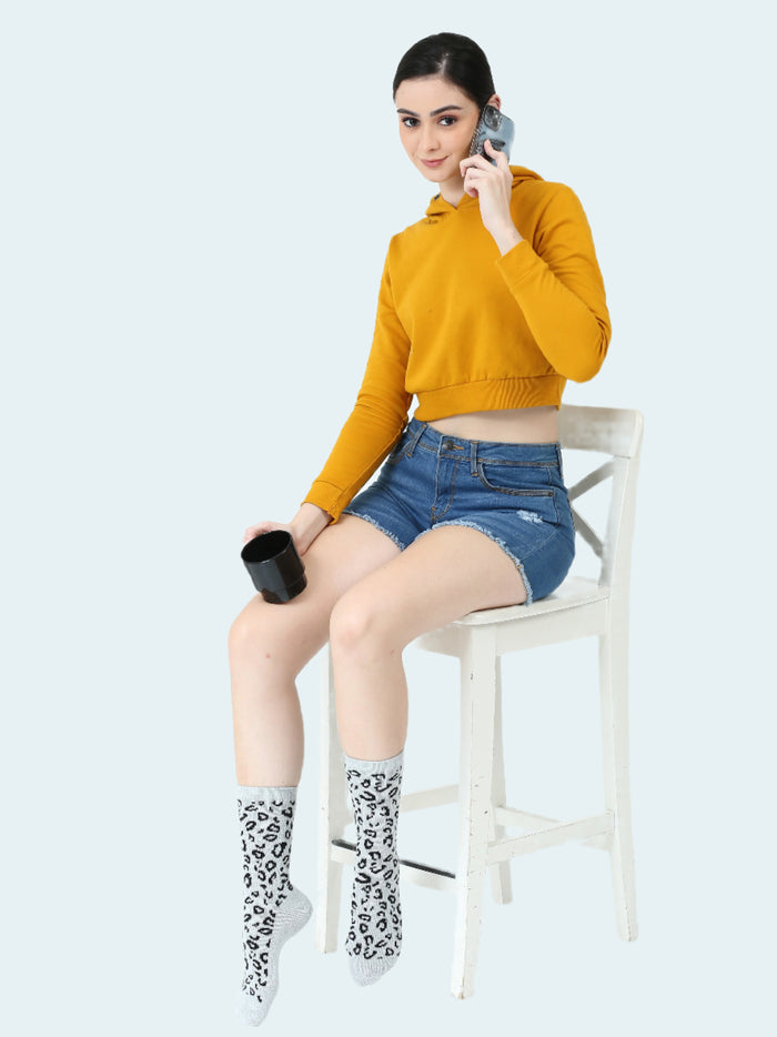 This image features a stylish young woman seated on a chair, She is wearing a vibrant mustard-colored crop top and denim shorts, adding a casual yet trendy touch to the scene.