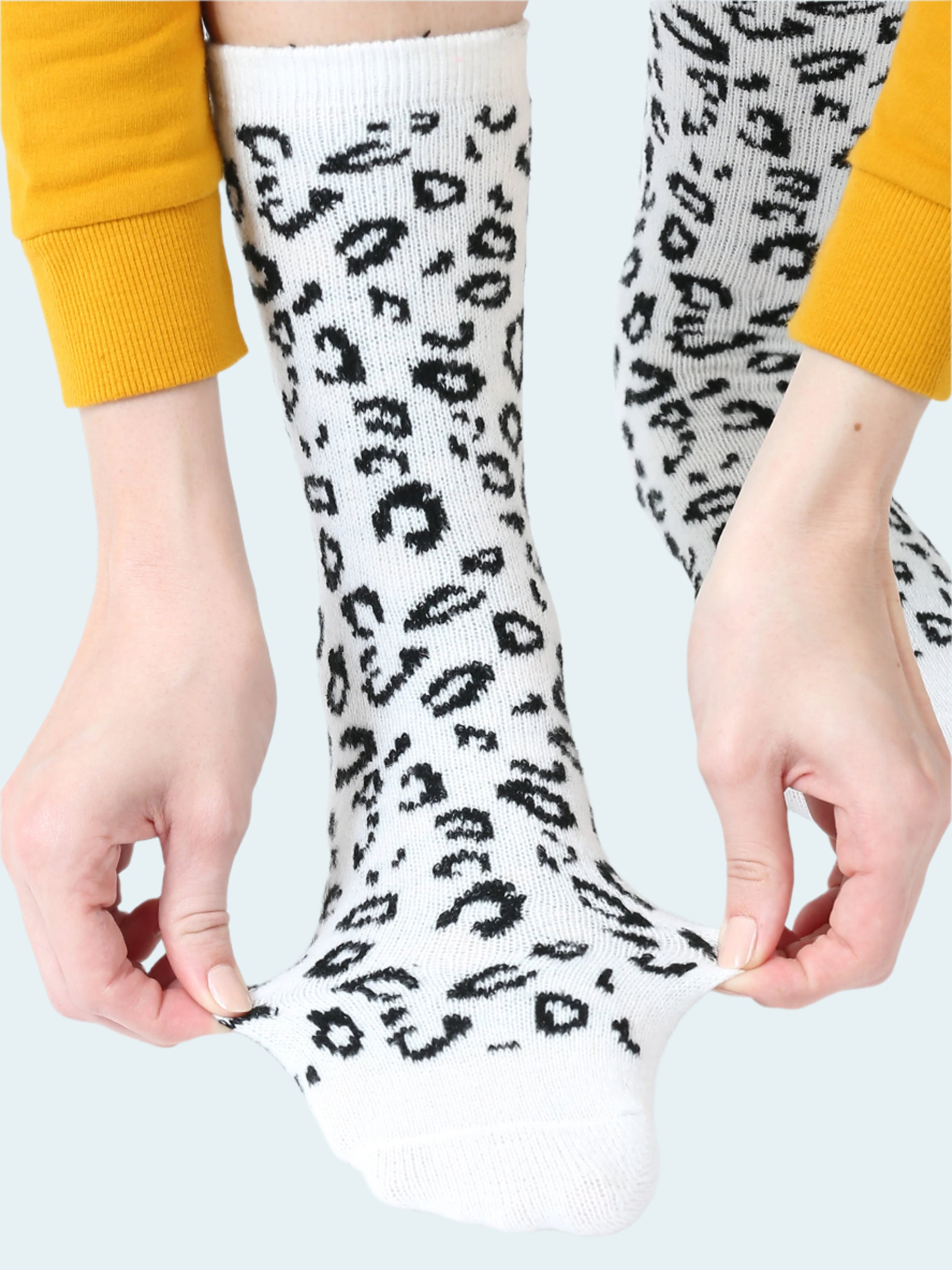 White socks with black leopard print held by a person wearing yellow sleeves.