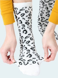 White socks with black leopard print held by a person wearing yellow sleeves.