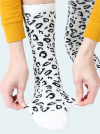 White socks with black leopard print held by a person wearing yellow sleeves.