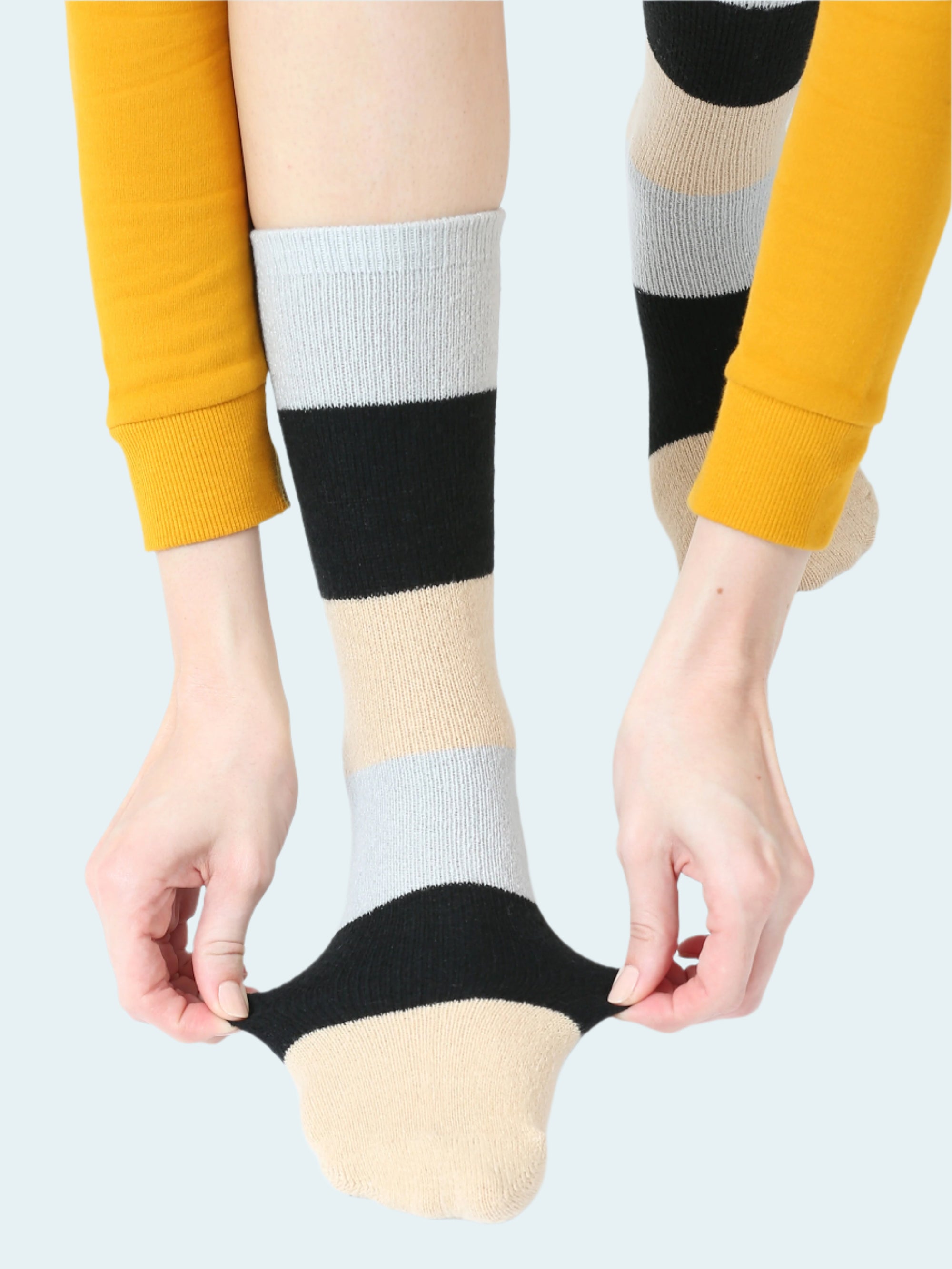 Color-blocked socks with black, white, and beige stripes worn by a person in a yellow sleeve.