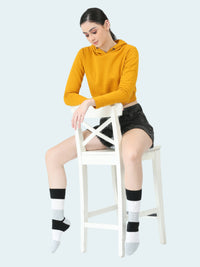 Woman sitting on a chair wearing mustard yellow hoodie, black skirt, and black and white socks.