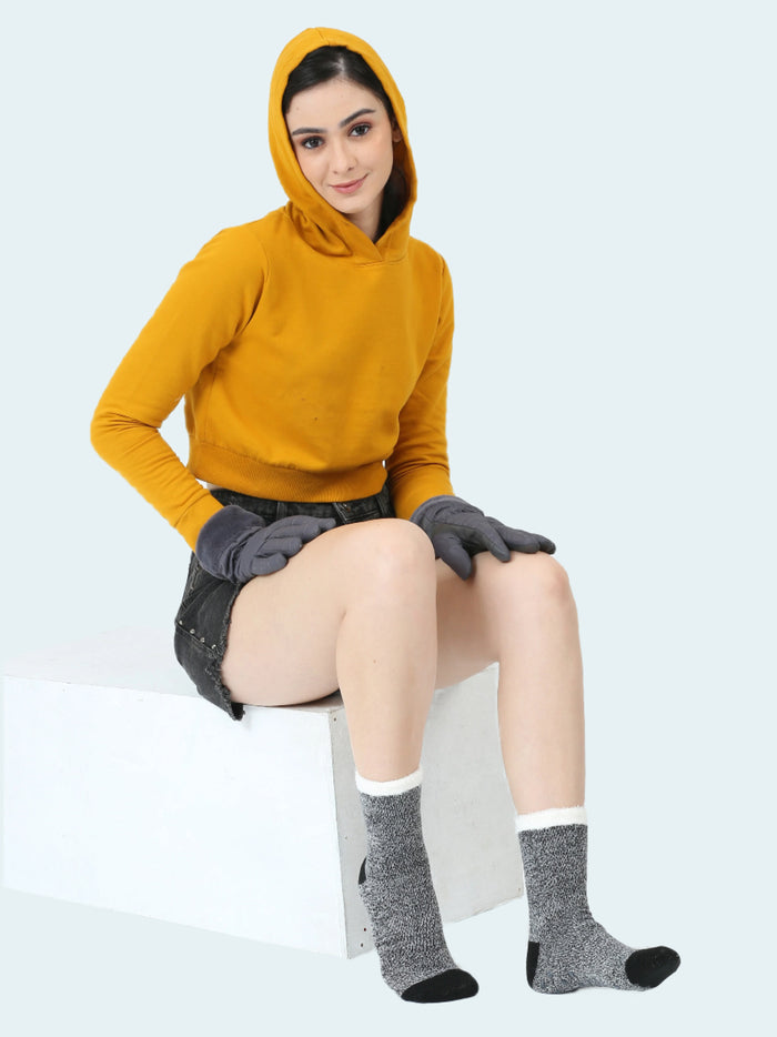 Person wearing a mustard yellow hoodie, gray gloves, and gray socks on a white background