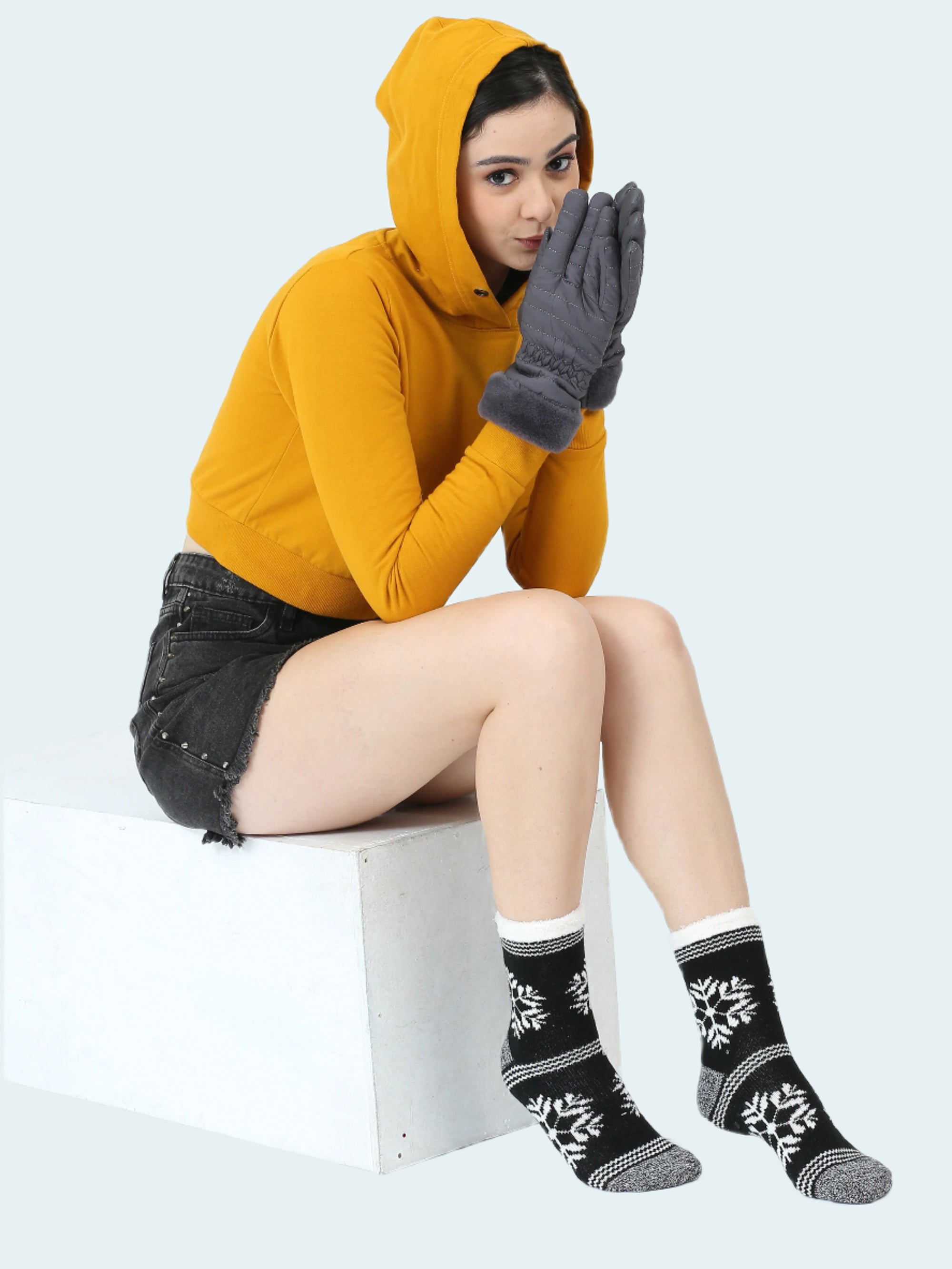 Person wearing a yellow hoodie and black floral socks sitting on a white stool.