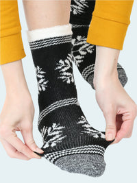 Black socks with white snowflake patterns worn by a person in yellow pants.
