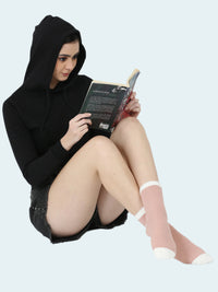 Person wearing a black hoodie and sheer socks, sitting and reading a book on a white background