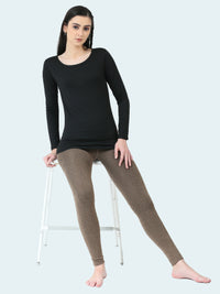 Woman wearing a black long-sleeve top and brown leggings sitting on a white stool against a white background.