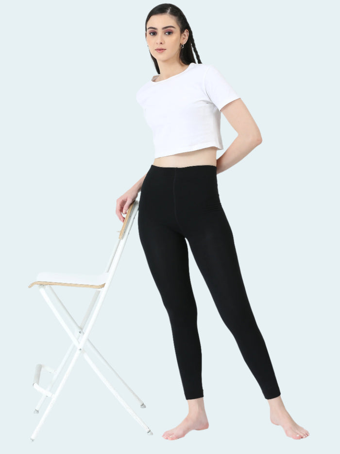 Woman wearing black leggings and a white crop top on a white background