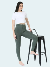 Woman wearing green leggings and a white crop top sitting on a black stool against a white background