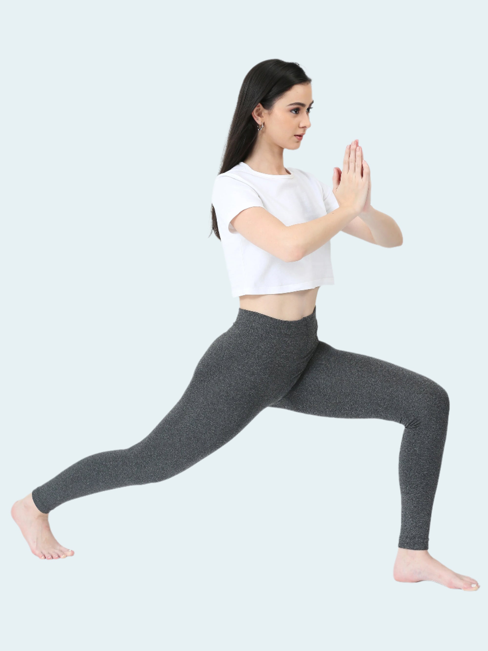 Woman in gray leggings and white shirt performing a yoga pose on a white background