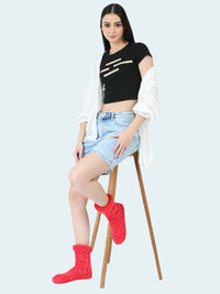 Woman wearing a black crop top, light blue denim shorts, and red socks sitting on a white box against a white background.