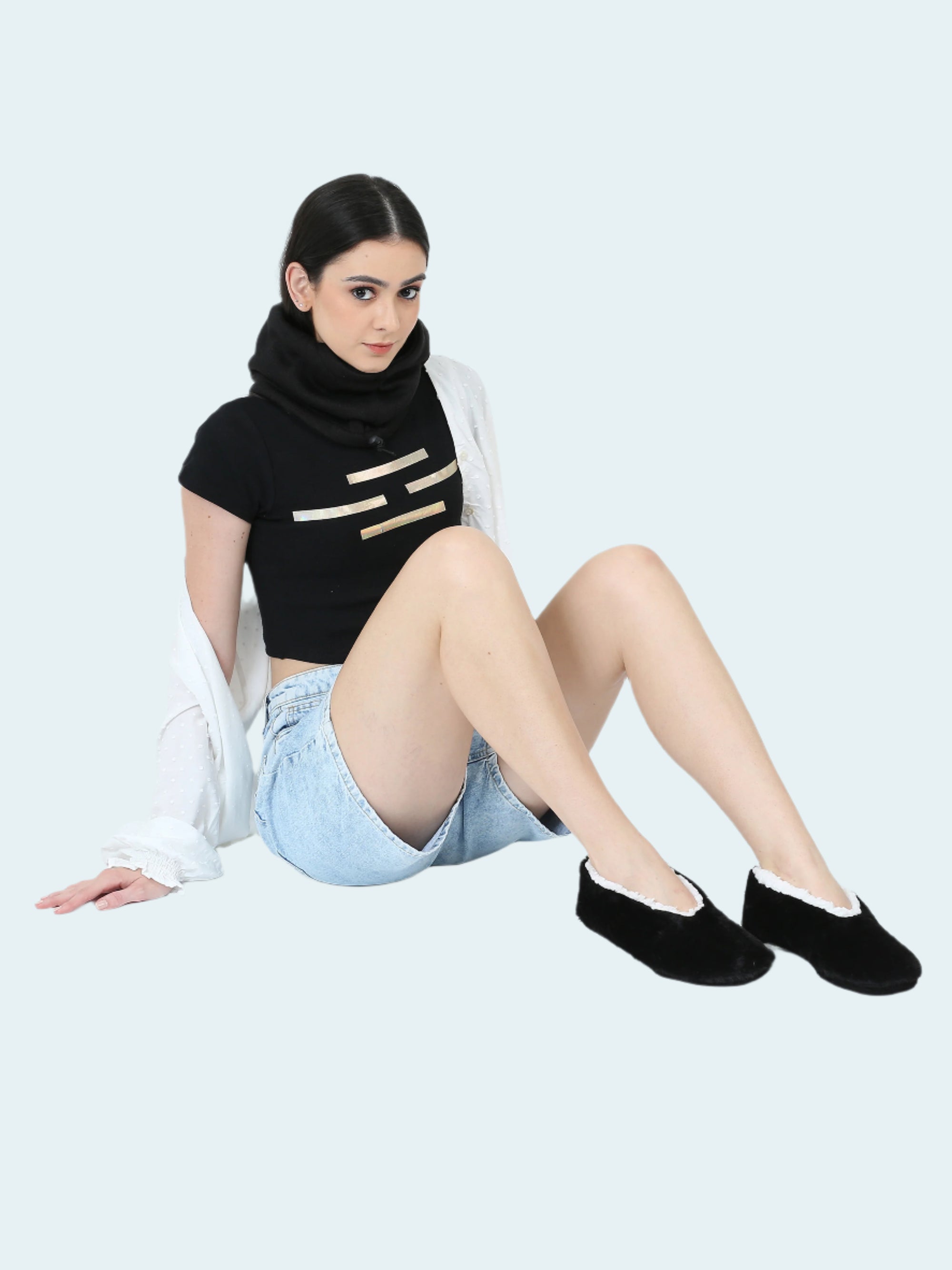 Woman wearing a black top with gold accents, denim shorts, and black slipper socks on a white background