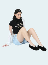 Woman wearing a black top with gold accents, denim shorts, and black slipper socks on a white background