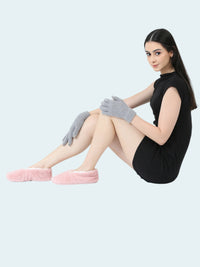 Woman sitting on a white floor wearing pink fuzzy socks and gray gloves, dressed in a black outfit.