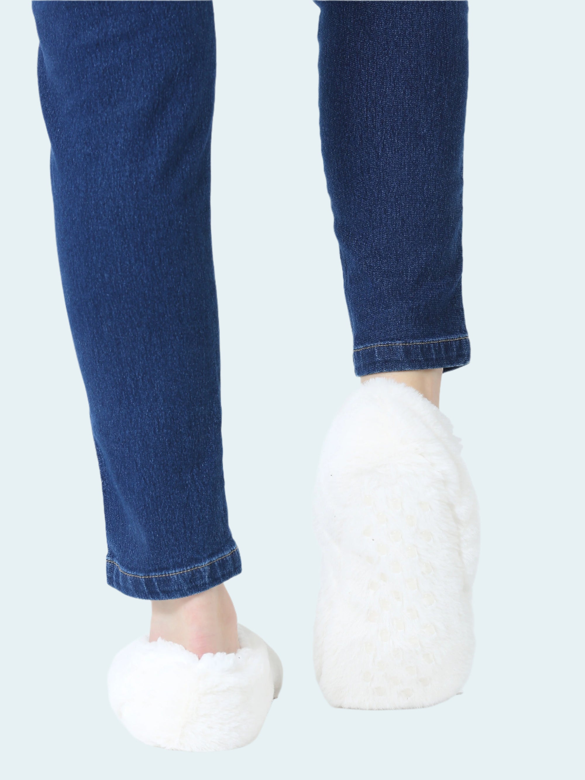 Person wearing blue jeans and white slipper socks on a white background