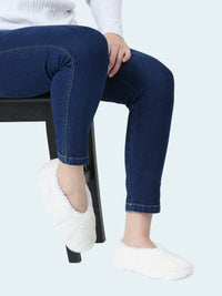 Person wearing blue jeans and white slipper socks sitting on a black stool against a white background