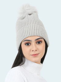 Person wearing a light gray knit beanie with a pom-pom on a white background