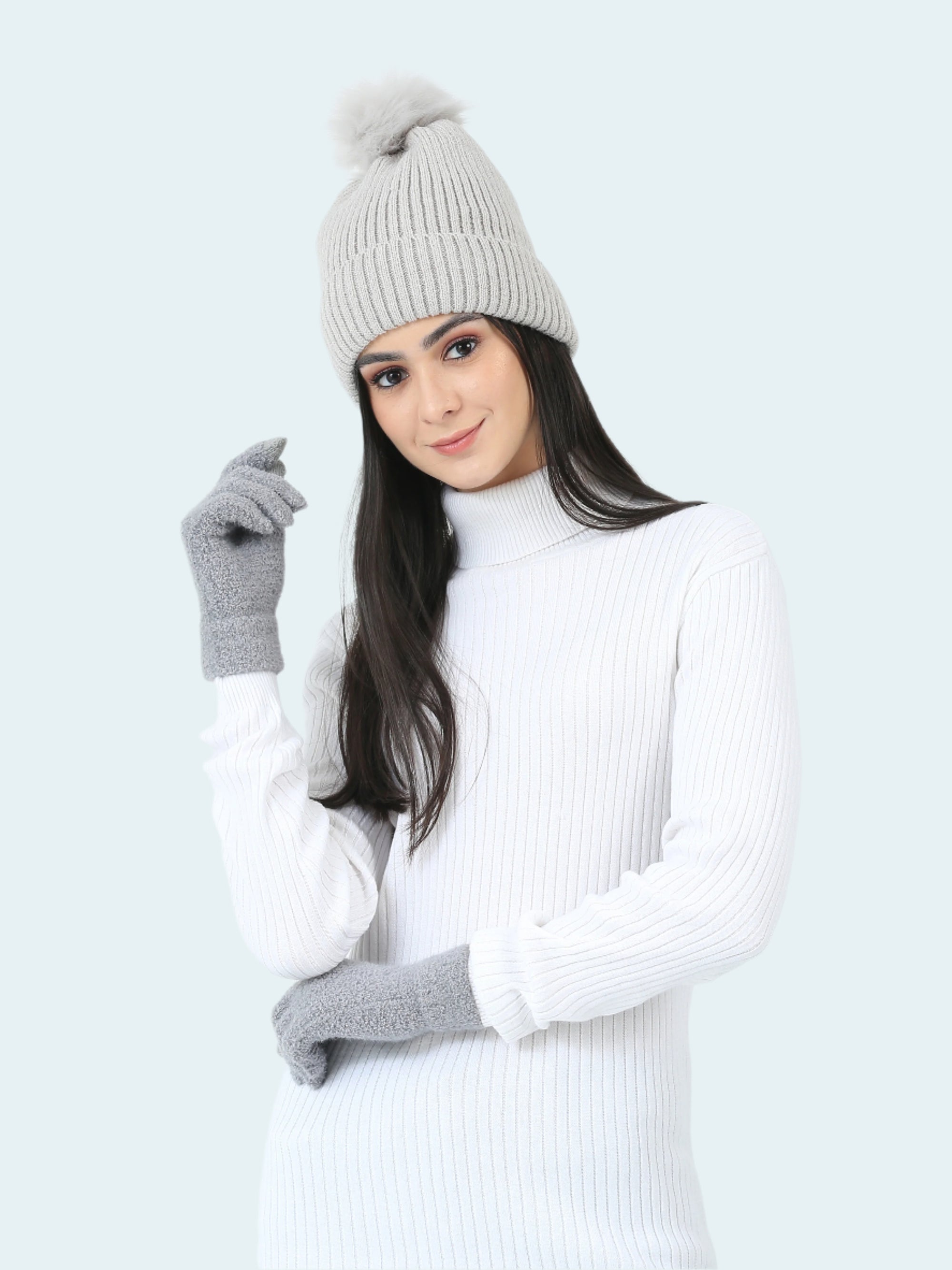 Woman wearing a gray knit hat, white sweater, and gray gloves on a light gray background